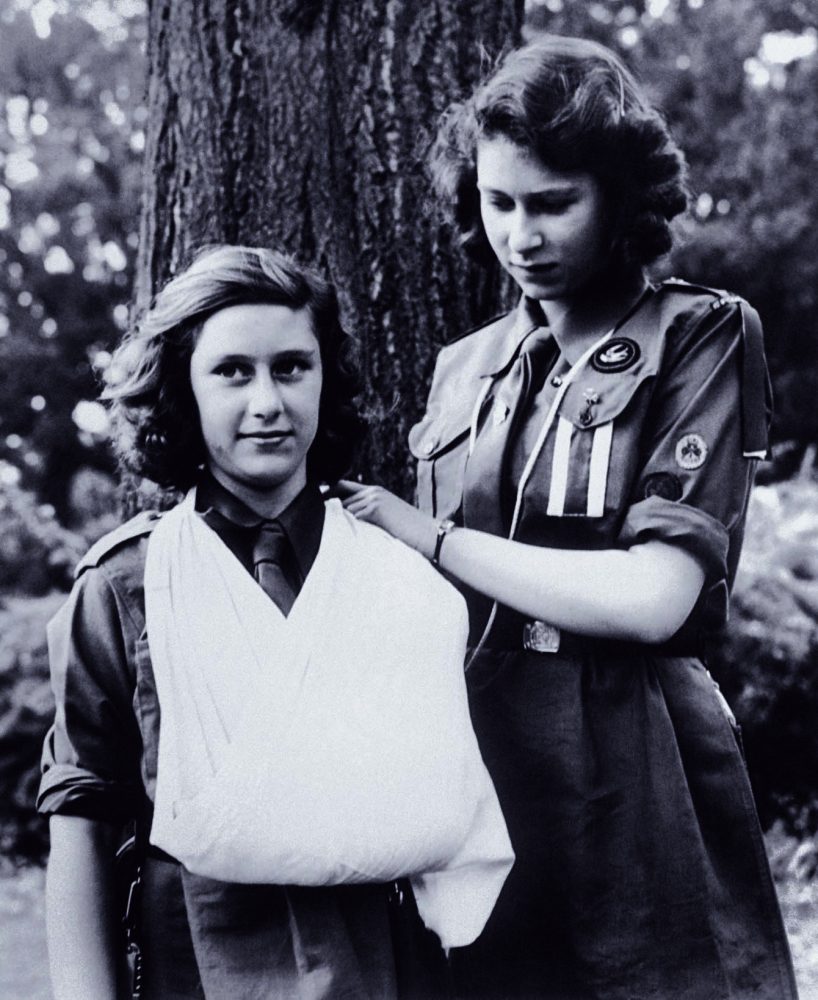 穿著女童軍制服的伊麗莎白（右）和瑪格麗特公主（左），攝於 1943 年 08 月，兩人正在練習包紮，從伊麗莎白的穿著可以看出她已經是女童軍的小隊長。圖片來源：美聯社
